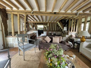 Ein rustikales Interieur mit freiliegenden Holzbalken, einer Steinwand, einem Essbereich und einer Couch mit Kissen.