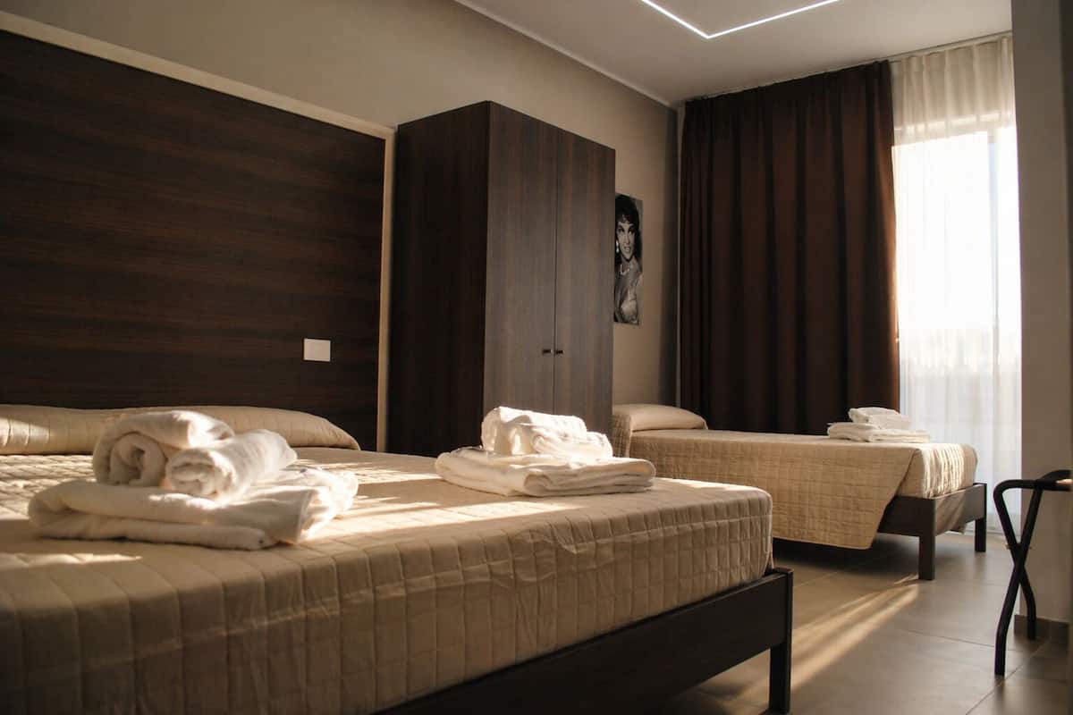 A hotel room with two beds, a wardrobe, and a window with curtains.