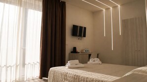 Una habitación de hotel con cama, televisión montada en la pared, escritorio con silla y armario.