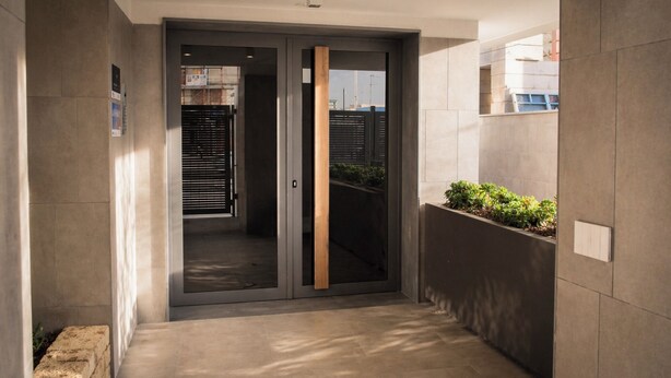 Un pasillo con una puerta corredera de vidrio que da a una habitación, un jardín vertical con vegetación y un suelo de baldosas.