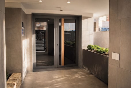 A corridor with a sliding glass door leading to a room, a planter with greenery, and a tiled floor.