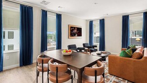 Ein modernes Wohnzimmer mit Esstisch, Stühlen, einer Couch und einem großen Fenster mit Vorhängen.
