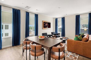 Ein modernes Wohnzimmer mit Esstisch, Stühlen, einer Couch und einem großen Fenster mit Vorhängen.