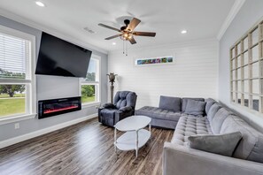 A living room with a fireplace, a ceiling fan, a grey sofa, and a white coffee table. - Chill Days, Fun Nights near Downtown Bay St. Louis. (Bay St. Louis)