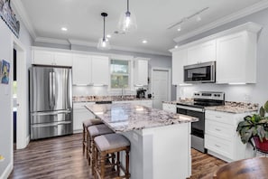 A modern kitchen with white cabinets, stainless steel appliances, a granite island, and bar stools. - Chill Days, Fun Nights near Downtown Bay St. Louis. (Bay St. Louis)