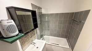 A bathroom with a bathtub, a sink, a mirror, and a heater.