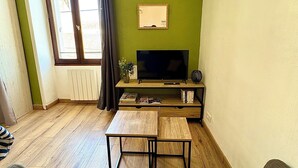 A living room with a TV, wooden furniture, a window with curtains, and a radiator.