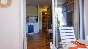 Una cocina con lavavajillas, un comedor con mesa y sillas, y vista a través de un ventanal.