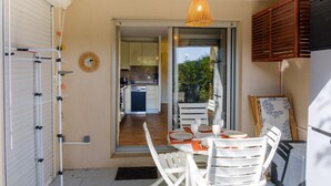Puerta abierta que da a una cocina con piso de madera, un comedor con sillas blancas y una mesa dispuesta para dos personas, y una lámpara colgante.