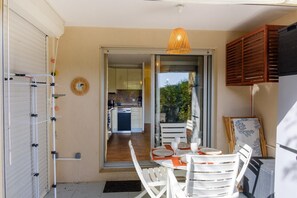 An open door leading to a kitchen with wooden flooring, a dining area with white chairs and a table set for two, and a hanging light fixture. - Apartment facing the port, 50m from the beach (Roquebrune-sur-Argens)
