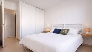 A bedroom with a bed, white headboard, bedside tables with lamps, and a wardrobe. - Charming apartment with terrace in Arès (Arès)
