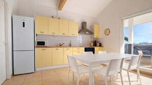 A modern kitchen with a white refrigerator, yellow cabinets, a white dining table with chairs, and a view of the outside through a large window. - Charming apartment with terrace in Arès (Arès)