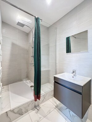 Ein modernes Badezimmer mit Dusche, Badewanne, Waschtisch mit Spiegel und Marmorboden.