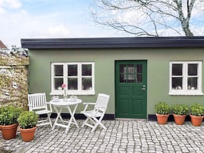 A green building with a green door, two windows, a table with chairs, and potted plants. - 4 Star Holiday Home in Ringkobing (Ringkobing)