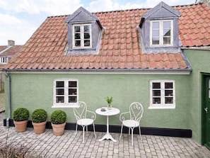 A green building with a tiled roof, two dormer windows, and a small patio with two white chairs and a table. - 4 Star Holiday Home in Ringkobing (Ringkobing)