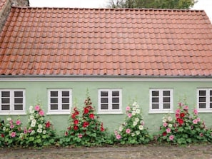 A building with a tiled roof and green walls, featuring windows and flowering plants. - 4 Star Holiday Home in Ringkobing (Ringkobing)