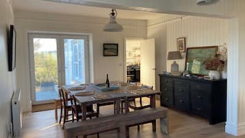 Un comedor con una mesa de madera dispuesta para cuatro personas, un banco y un aparador oscuro con una lámpara.