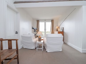 A room with two white-covered chairs, a small table with a lamp, a telescope, and a wooden chair. - Arfryn (Amlwch)