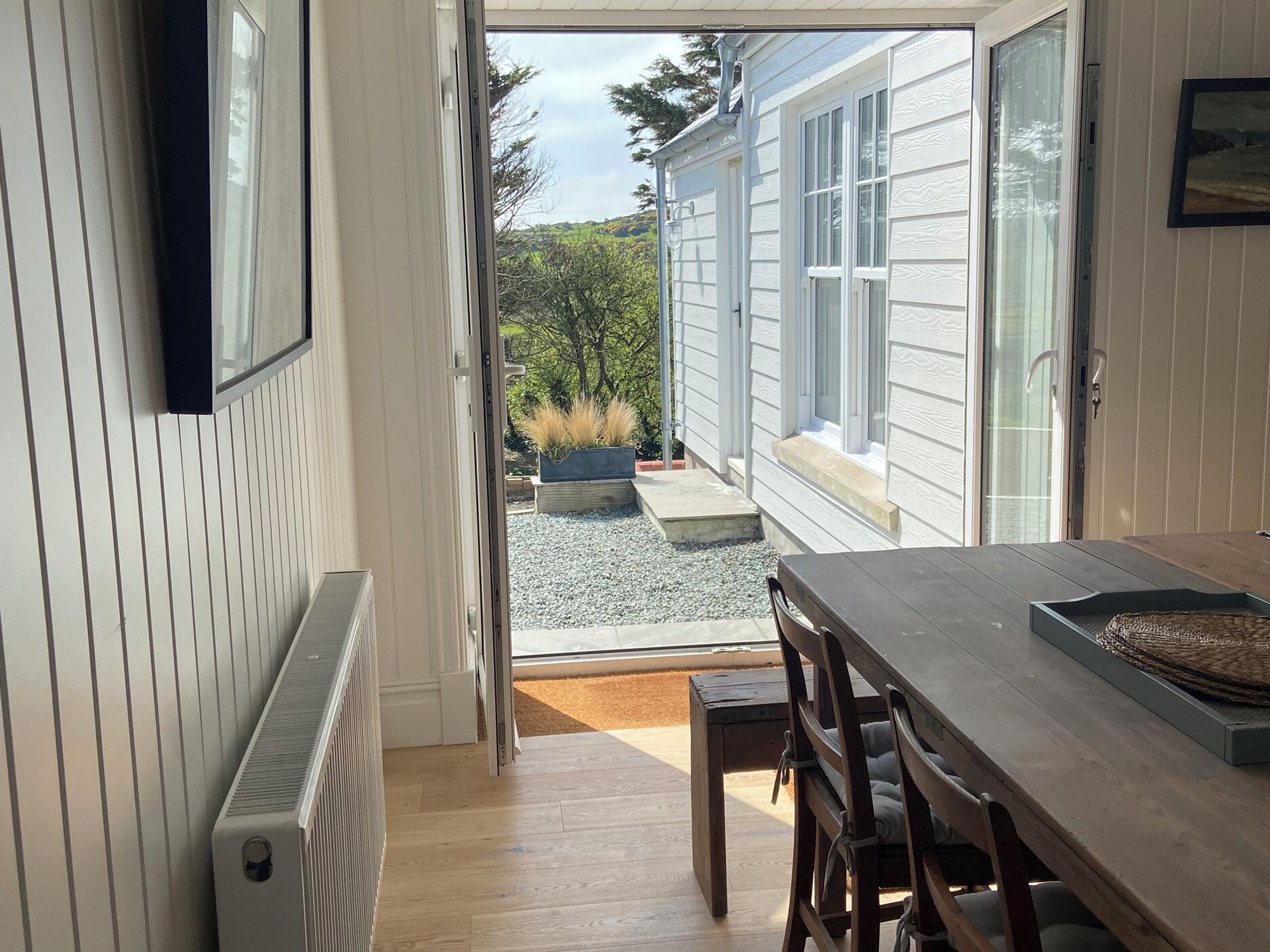 A room with a wooden table and chairs, a radiator, and a view of a garden through a sliding glass door.