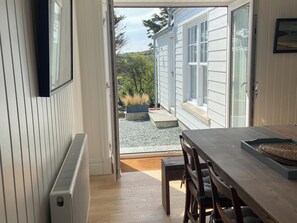 A room with a wooden table and chairs, a radiator, and a view of a garden through a sliding glass door. - Arfryn (Amlwch)
