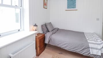 Un dormitorio con una cama individual, un radiador, un mueble de madera pequeño, un cuadro en la pared y una ventana con cortinas.