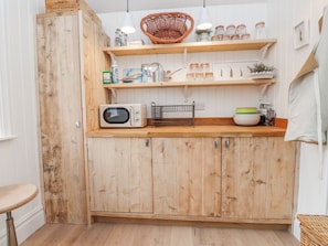 Una cocina con armarios de madera, microondas, estantes con frascos y una cesta de mimbre.