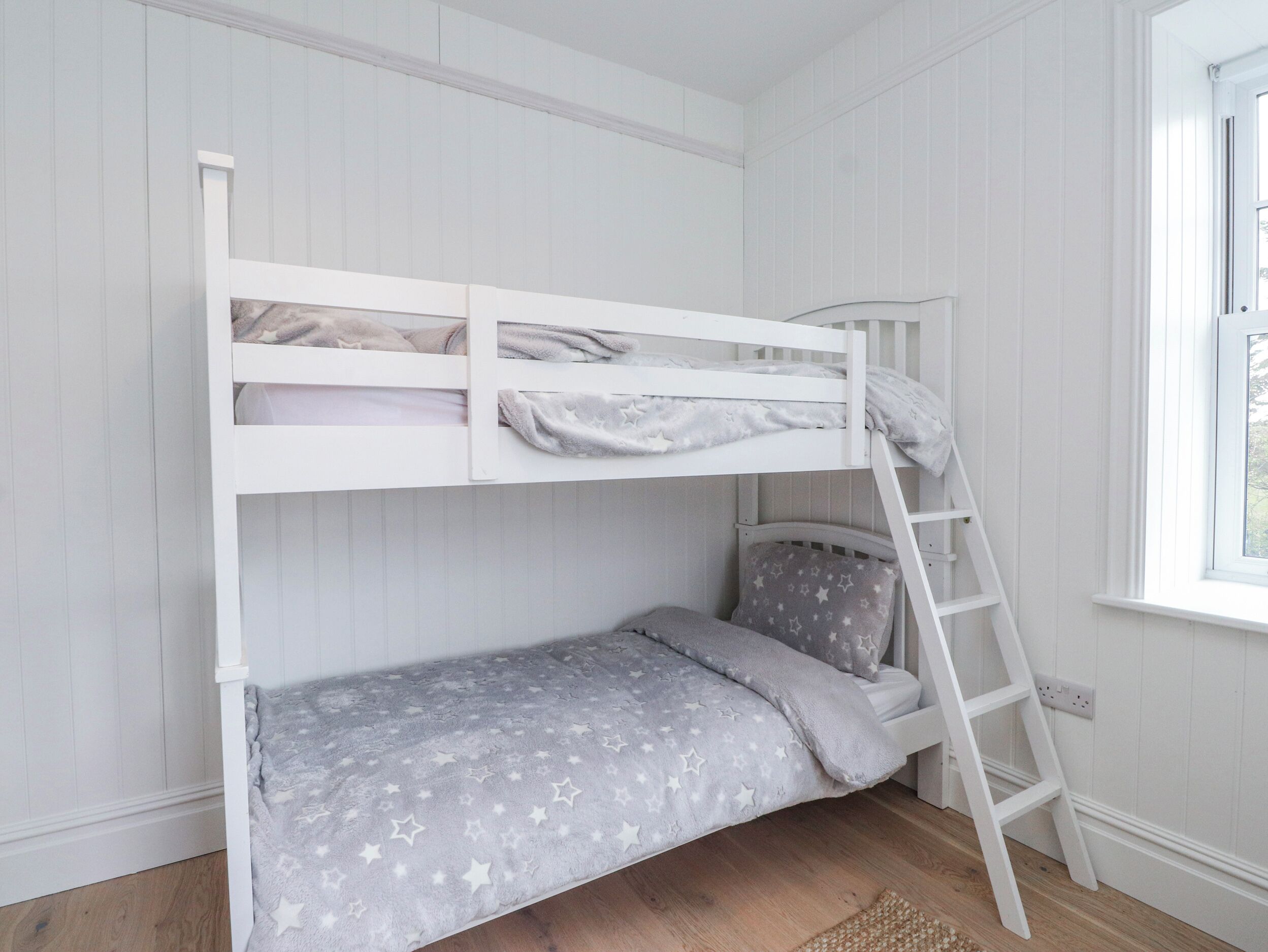 A bunk bed with a ladder, a window with a view, and a wooden floor.