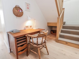 A wooden desk with a lamp, a chair, a bookshelf, a wicker basket, and a staircase.
