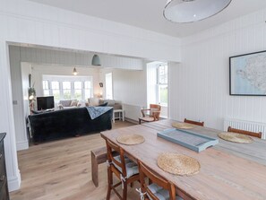 A spacious room with a wooden dining table, chairs, a sofa, and a television. - Arfryn (Amlwch)