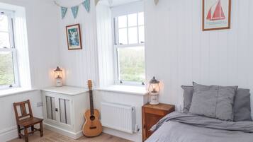 Un dormitorio con cama, una guitarra, una silla y dos ventanas con cortinas.