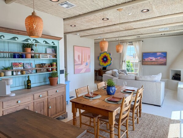 A dining area with a wooden table and chairs, a kitchen with a blue cabinet, and a living area with a sofa and a painting.