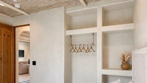 Une chambre à coucher avec un lit, une armoire en bois, un mur blanc avec des étagères et un porte-vêtements.