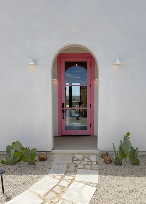 A pink door with a glass panel, white walls, and two wall-mounted lights.