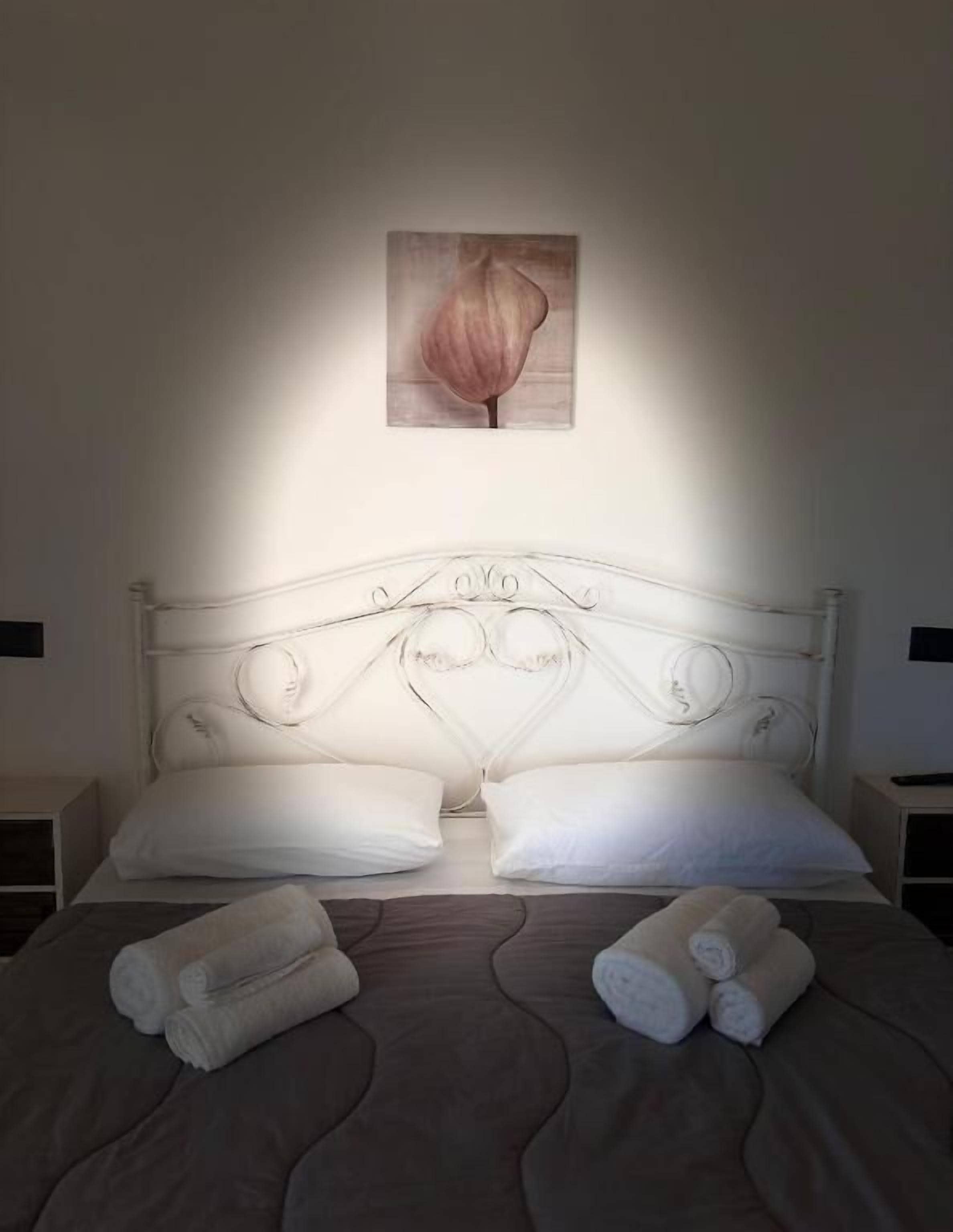 A neatly made bed with white linens, two pillows, and rolled towels on the bed.