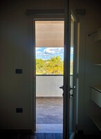 An open door leading to a balcony with a view of trees and a clear sky.