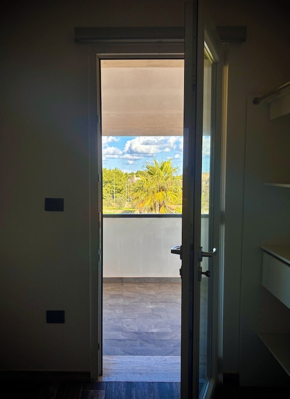Une porte ouverte donnant sur un balcon d’où l’on peut admirer les arbres et un ciel dégagé.