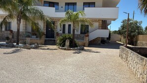 A modern building with a stone facade, a central entrance, and a small courtyard with palm trees and a fountain. - B&B Helios (Nardò)