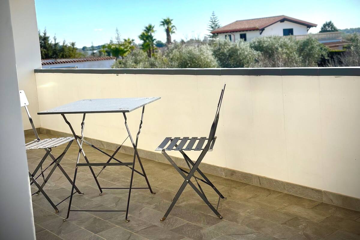 A patio with a table and chairs, a view of a house, and a clear sky.