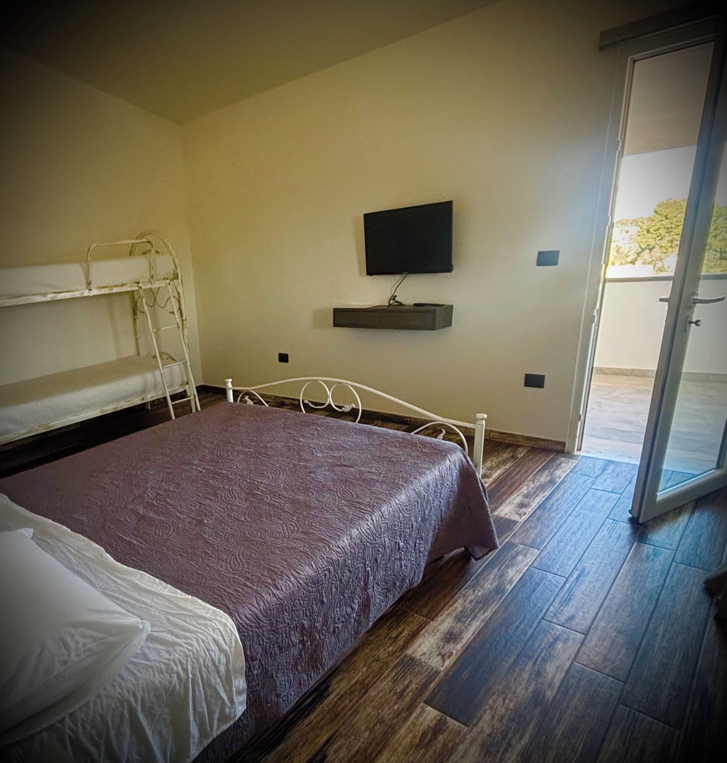 A room with a bunk bed, a flat-screen TV mounted on the wall, and a sliding glass door leading to an outdoor area.