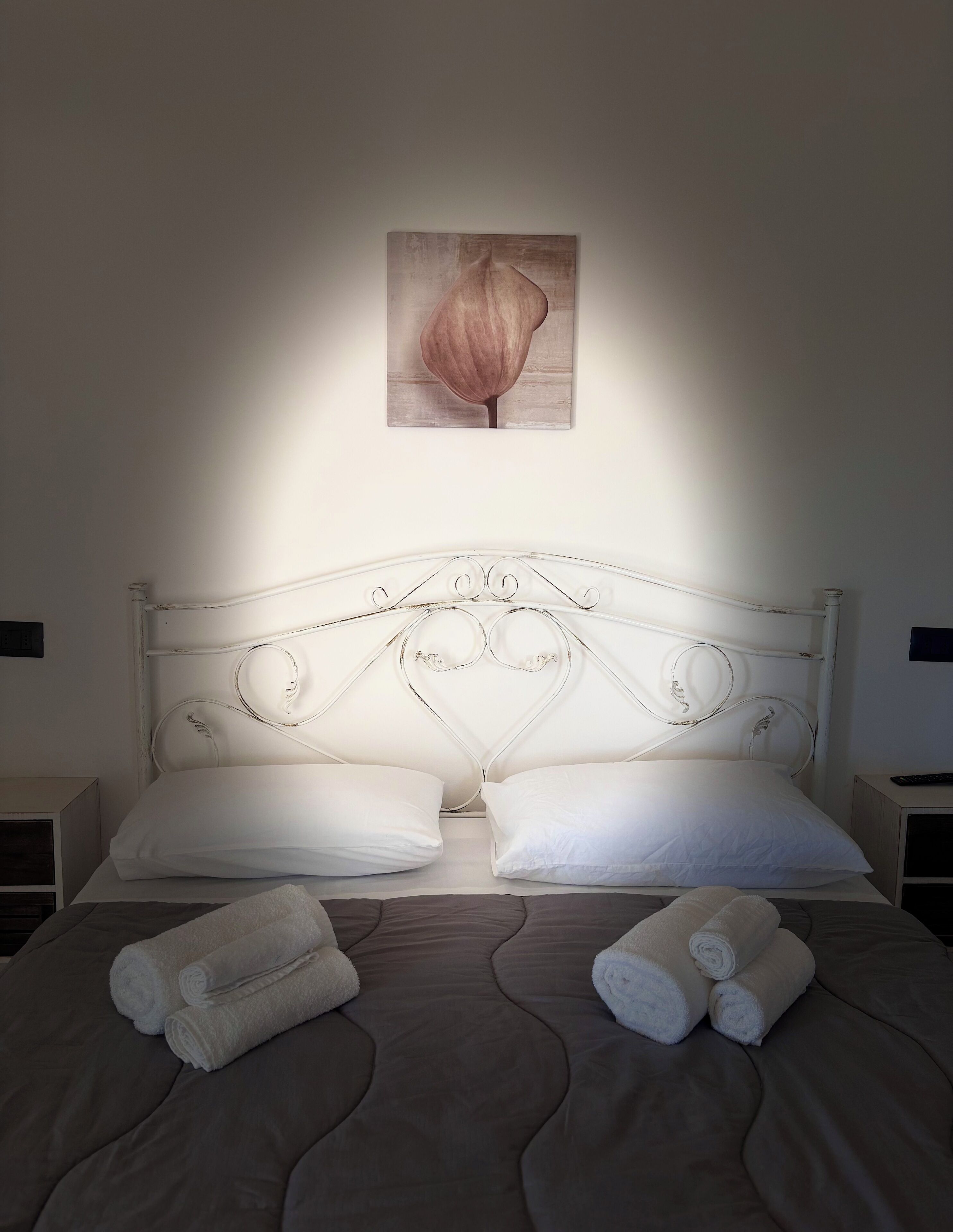A neatly made bed with white linens, a decorative headboard, and a single artwork above it.