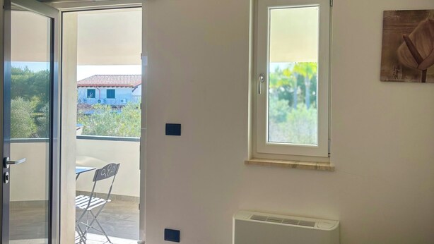 A bedroom with a bed, a window, a radiator, and a balcony with a table and chairs. - B&B Helios (Nardò)