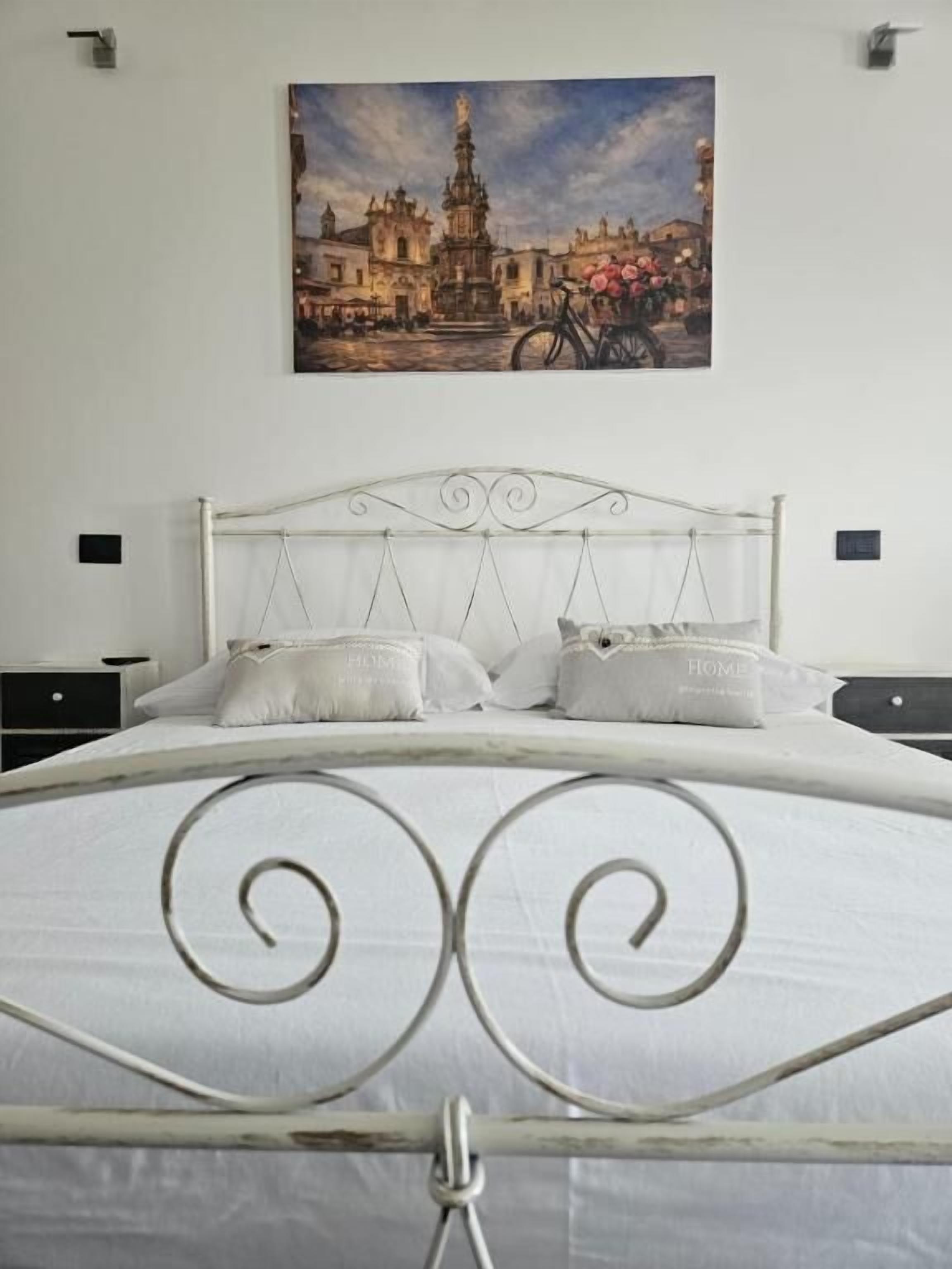 A bedroom with a metal bed frame, white bedding, and a painting of a cityscape on the wall.