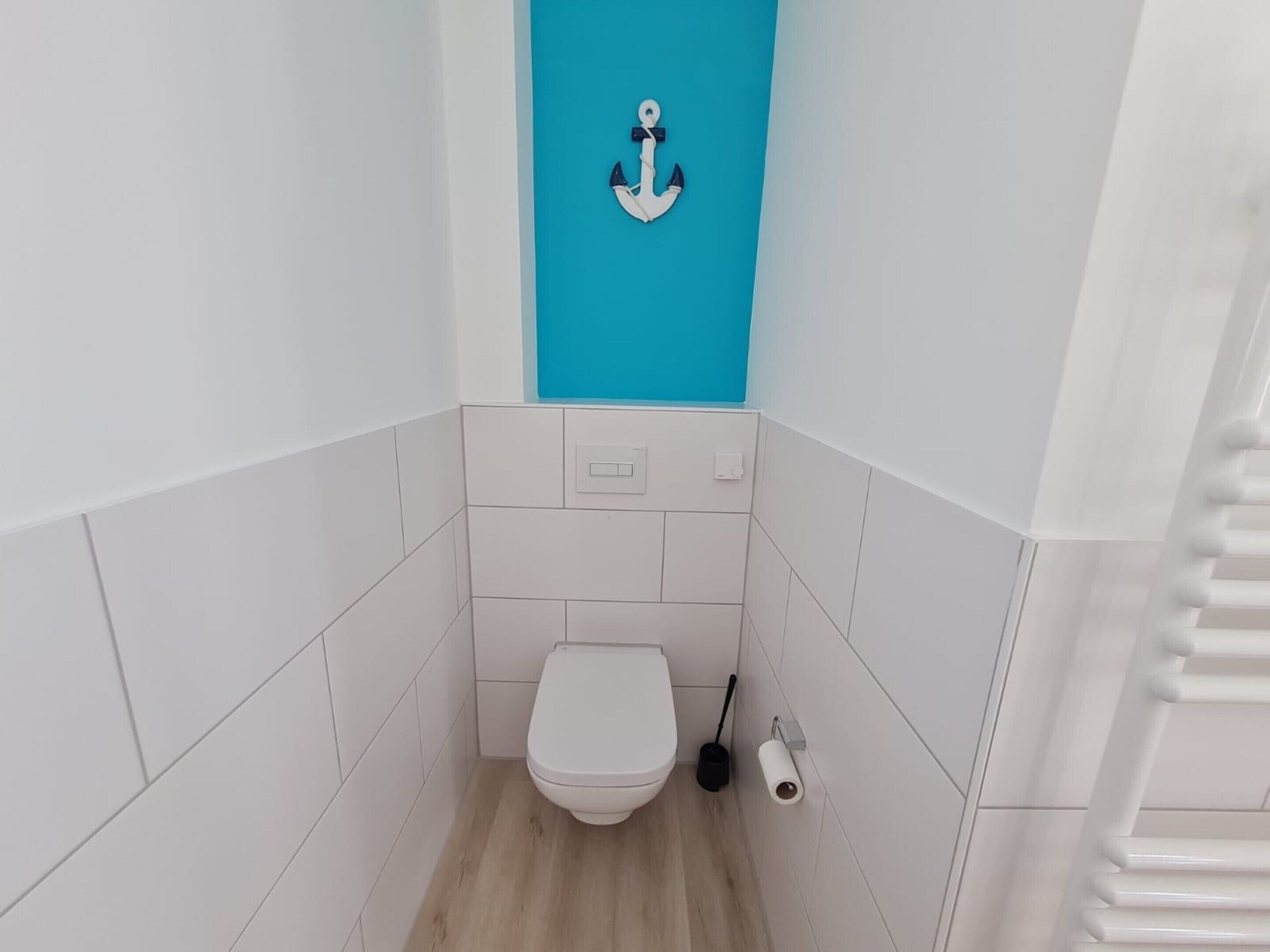 Um banheiro pequeno e estreito com azulejos brancos, vaso sanitário branco, parede azul decorativa e porta-toalhas branco.