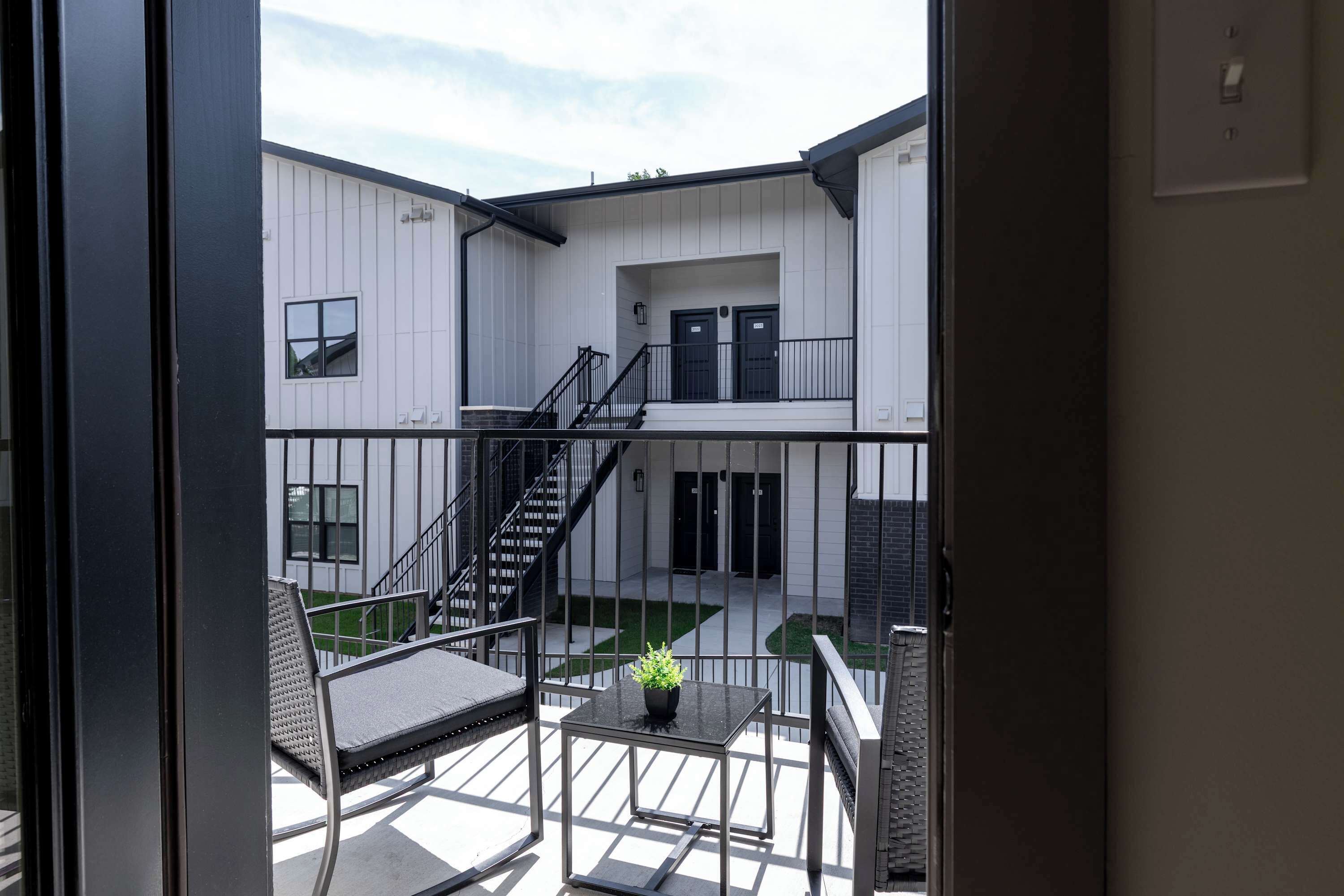 Un bâtiment moderne doté d’un balcon, d’un escalier et d’une petite table sur laquelle est posée une plante.