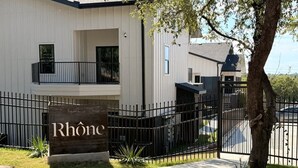 Une entrée fermée par un portail, sur laquelle on peut lire l’inscription « Rhône », et un bâtiment moderne doté d’un balcon.
