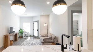 Un salon moderne avec un comptoir en marbre, un canapé, un téléviseur et une lampe sur pied.