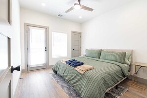 A bedroom with a bed, a ceiling fan, and a door with blinds.