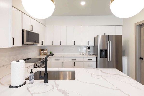 A modern kitchen with white cabinets, stainless steel appliances, a marble countertop, and pendant lighting.