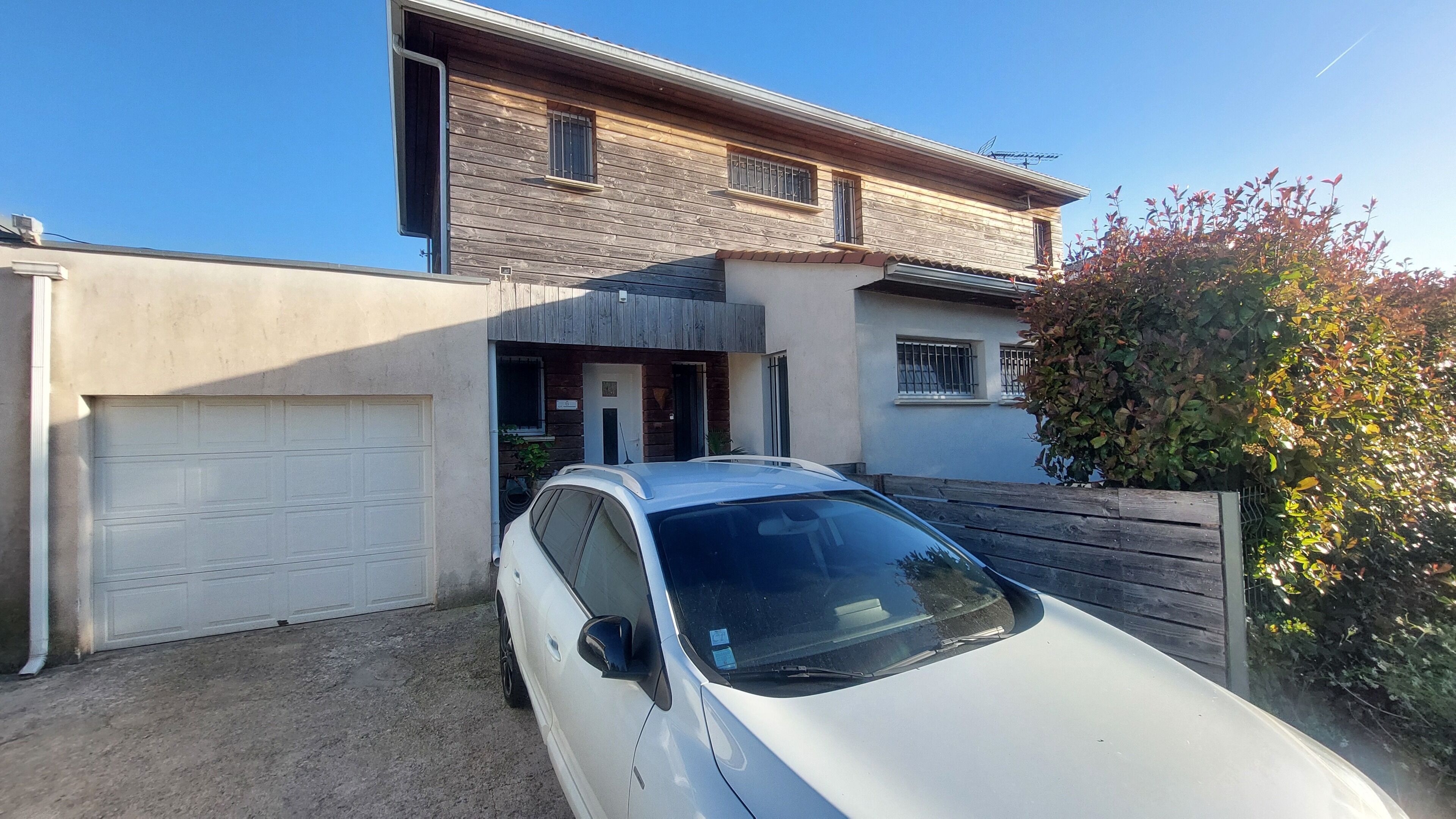 Une maison à deux étages avec un garage, une allée et une voiture blanche garée dans l’allée.