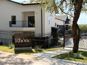 A gated entrance with a sign reading 'Rhône' and a modern building with a balcony. - [R17] 1BD/1BA Condo, Brand New, Furnished & Work-Ready! (Austin)